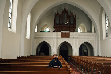 Priest sitting in church pew reading bible