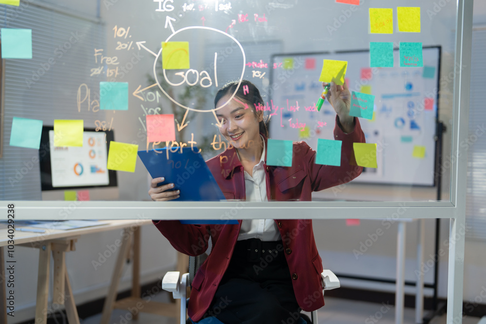 Poster young manager is using colorful sticky notes to brainstorm ideas and organize her tasks on a transpa