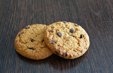 two chocolate chip cookies with chocolate chips on a wooden surface macro