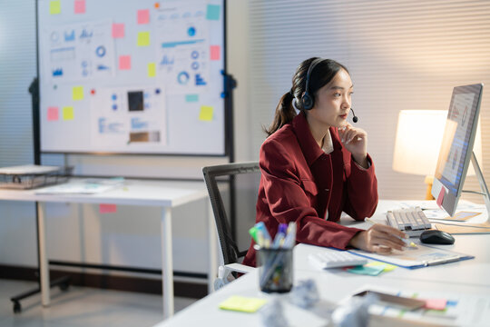 Young professional wearing a headset is working late in the office, reviewing data and spreadsheets while on a conference call