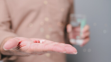 Supplements, Persons hand holds two capsules and tablet, accompanied by glass of water, symbolizing...