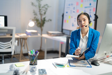 Focused asian businesswoman taking notes at desk in busy office, using technology and communication skills for success in corporate world