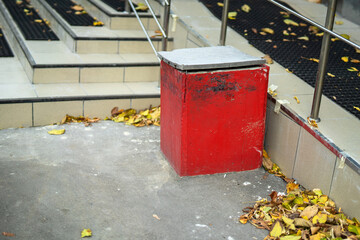 striking red concrete trash bin positioned beside an inviting staircase. This juxtaposition highlights urban life, waste management, and aesthetic contrast in public spaces