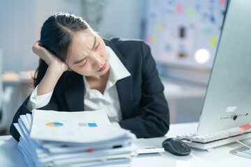 Exhausted businesswoman overwhelmed by heavy workload at office desk, surrounded by paperwork and...