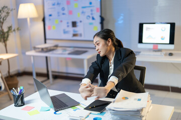 Tired businesswoman stretches at her desk in a late-night office, taking a break to relax and focus on health while surrounded by paperwork and technology