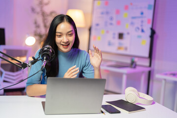 Asian woman is recording a podcast from her home studio, talking and gesturing while engaging with her audience online