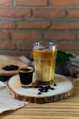 Glass of cappuccino with foam and espresso in natural background and wood elements