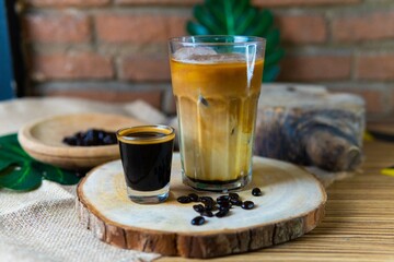 Glass of cappuccino with foam and espresso in natural background and wood elements