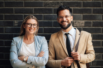 Business partners smiling while standing against a black brick wall