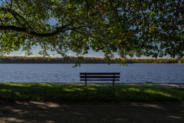 AUTUMN LANDSACAPE - A bench in park by lake under colorful leaves on a sunny day © Wojciech Wrzesień