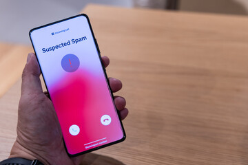 Hand holding smart phone with suspected spam incoming call warning from mobile network.