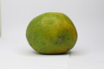 A close-up of a green citrus fruit on a white background. The fruit has a rough, textured skin with some yellow spots.