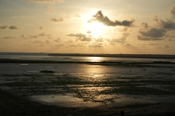 Obraz premium Golden sunset over calm sea with clouds reflecting on wet sand