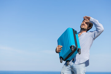 Happy and euphoric single young adult man with his blue travel suitcase with the background of blue...