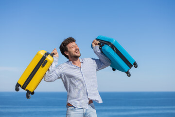 Happy and euphoric single young adult man with his yellow and blue travel suitcases with the...