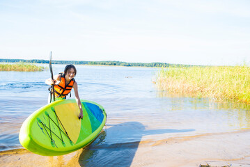 boy carries stand up paddle board from lake to shore after riding	