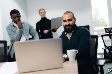 Diverse group of professionals concentrating on laptop screen, suggesting teamwork and...