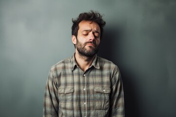 Portrait of a tender man in his 30s dressed in a relaxed flannel shirt in front of minimalist or empty room background