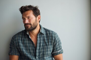 Fototapeta premium Portrait of a tender man in his 30s dressed in a relaxed flannel shirt in minimalist or empty room background