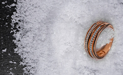 A close-up of a worn, gold ring with small diamonds lying on top of a pile of white salt crystals...