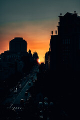 A vibrant sunset over a city street. The detailed round shape of the yellow-orange sun is directed precisely to the center of the street. An amazing rare phenomenon in the city.
