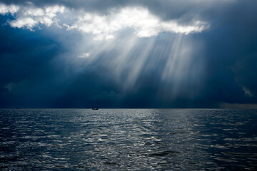 Dramatic seascape with towering clouds casting long shadows over the ocean, as the sun dips below the horizon