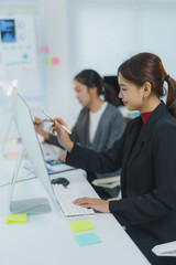Two businesswomen are working together on a project, collaborating and using computers in a modern office setting
