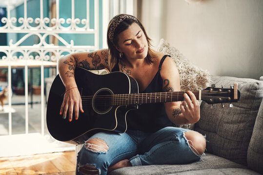 Woman, relax and guitar in home for music, practice and learning chords on sofa. Musician, string instrument and strumming in living room with talent, pitch development or rehearsal for performance