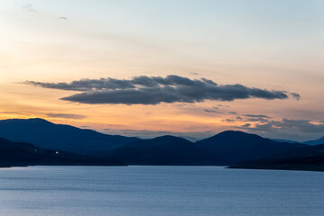 lake surrounded by gentle mountains after sunset, bright sky and water