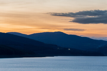 lake surrounded by gentle mountains after sunset, bright sky and water
