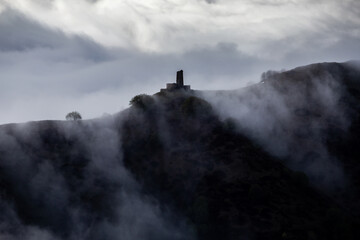 medieval tower on mountain above clouds, with snowy mountain picks, cloud flows over mountain ridge
