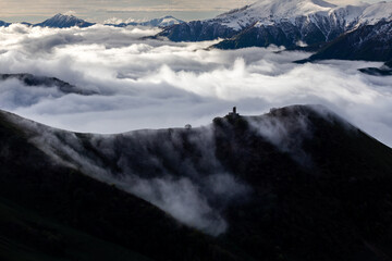 medieval tower on mountain above clouds, with snowy mountain picks, cloud flows over mountain ridge