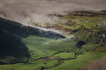 village in mountains close up from above, green meadows and clouds