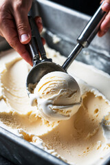 Fototapeta premium Vanilla ice cream scoop being served from a metal container with stainless steel scoop, close-up
