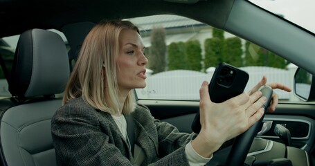 A stylish woman with earphones is driving around the city on a sunny day. She is talking on the mobile phone