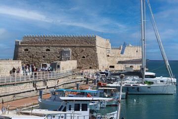 Tourists walking near koules fortress at the old venetian harbour entrance in heraklion, crete, greece