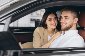 Portrait of smiling beautiful couple sitting in modern luxury car, happy excited young man and woman buying new car in dealership.