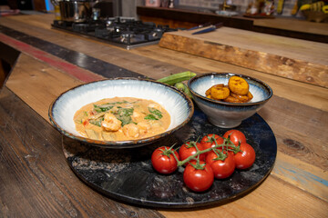 A bowl of delicious West African stew surrounded by the ingredients used to make the dish on a wooden kitchen work top