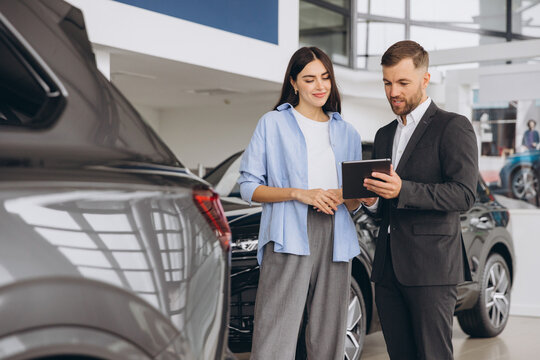 Young woman customer female buyer client wears shirt consult with salesman hold tablet choosing auto want to buy new automobile in car showroom vehicle salon dealership store motor show.