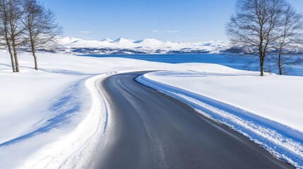 Fototapeta premium A winter road winds through snowy fields and trees in Iowa, with a glistening lake visible in the distance under a stunning sky