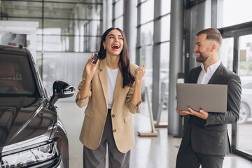 Charming young Caucasian woman holding keys of new car and show fist and say yes in modern car...