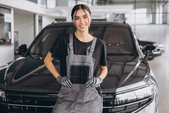 Portrait of young woman, professional female mechanic smiling at camera standing in auto repair shop. Car service, repair, maintenance and people concept.