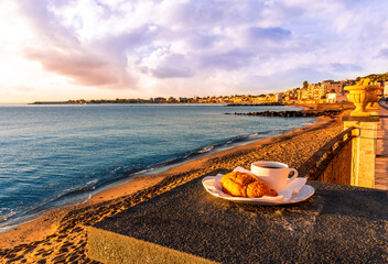 concept of street outdoor breakfast with a cup of tea or coffee on a morning coast during sunrise. landscape of city embarkment with sea water and cloudy sky on background