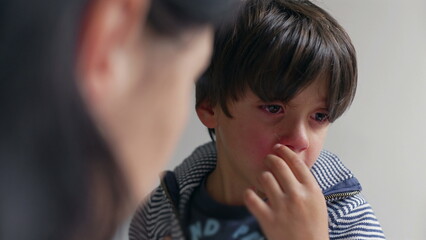 Mother talking while her son listens, visibly upset and emotional, with tears in his eyes. The mother offers comfort and guidance in a supportive home environment