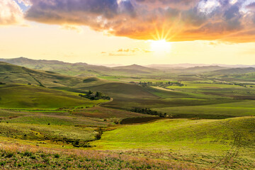 beautiful green valley with green fields with green spring grass with nive hills and mountains and scrnic colorful cloudy sunset on background of landscape