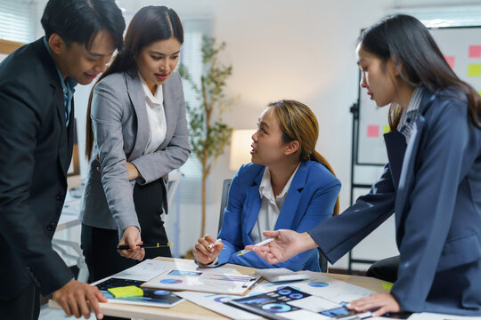 Team of asian professionals in business attire are having a discussion around a table, analyzing financial data and strategizing on a project