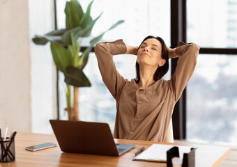 Successful Deal. Satisfied female office worker leaning on chair with hands behind head, relaxing...