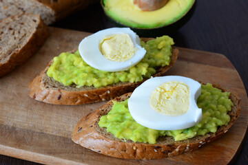 a wooden cutting board with avocado toast with mashed avocado on it and egg 