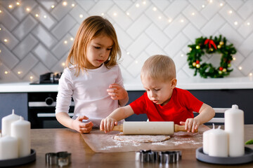 The brother and sister are rolling out gingerbread dough for cookies at Christmas