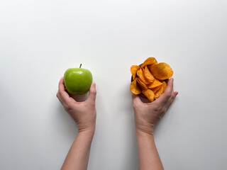 Hands holding green apple and potato chips on the white background.  Choosing between healthy nutritious fruits and unhealthy high-calorie foods.